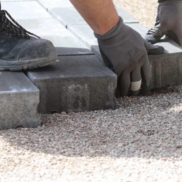 A person putting pavers onto a path of sand.